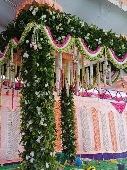 A close-up of a traditional mandap arch, showing the detailed floral work with green leaves and pink and white flowers.