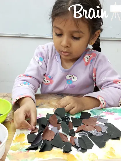 This student is carefully selecting and placing paper pieces, learning about color, shape, and texture. Sensory craft sessions like this are fundamental to our early childhood learning program.