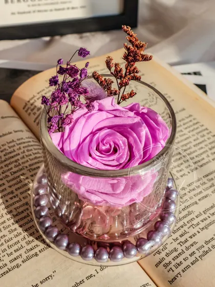 The preserved rose is set in a ribbed glass jar with a pearl-accented base.