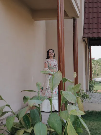The bride smiles brightly while posing for a portrait amidst lush green plants at her wedding venue.