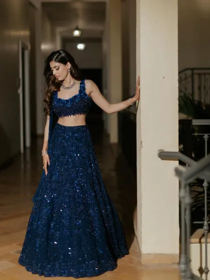 A full-length portrait of the bride in her Sangeet attire. The deep blue lehenga is a showstopper, and the makeup is pure glamour.
