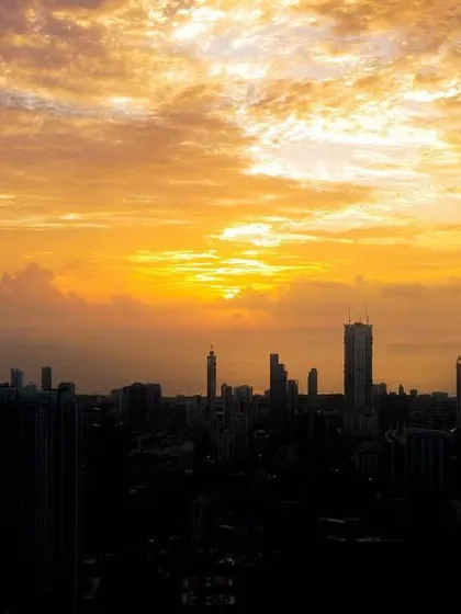 A cluster of clouds catches the golden light of the setting sun, creating a dramatic, fiery sky over a silhouetted Mumbai.