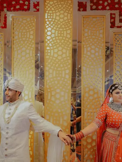 A creative couple portrait using reflections. The bride and groom hold hands, creating a symmetrical and artistic shot against a modern, decorative backdrop.