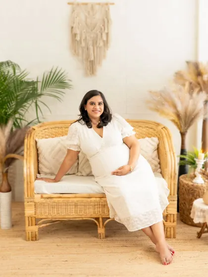 A beautiful solo portrait of a mom-to-be in a simple white dress, seated gracefully in our natural-themed studio.