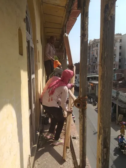 Beginning the meticulous restoration of a 19th-century haveli's facade, with workers carefully removing damaged sections while preserving the structure.