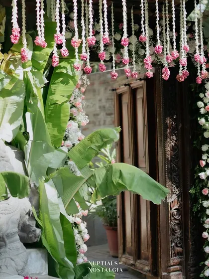 An entrance decorated with banana leaves and hanging pink and white floral strings.