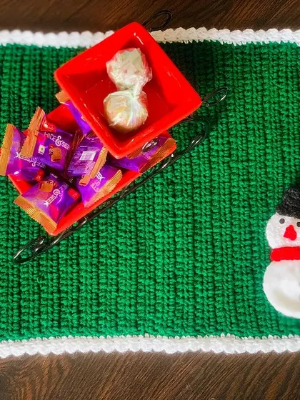 This rectangular Christmas placemat in festive green is decorated with a small snowman appliqué. It's a fun and practical piece for your holiday table setting.
