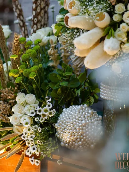 A close-up of a floral arrangement that perfectly captures the theme. It combines white roses, green foliage, dried wheat, and a striking pearl-covered sphere for a mix of rustic and luxe.