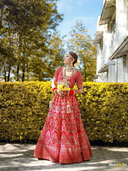 A stunning outdoor portrait of the bride in her red lehenga, holding a bouquet of yellow flowers that adds a beautiful pop of color.