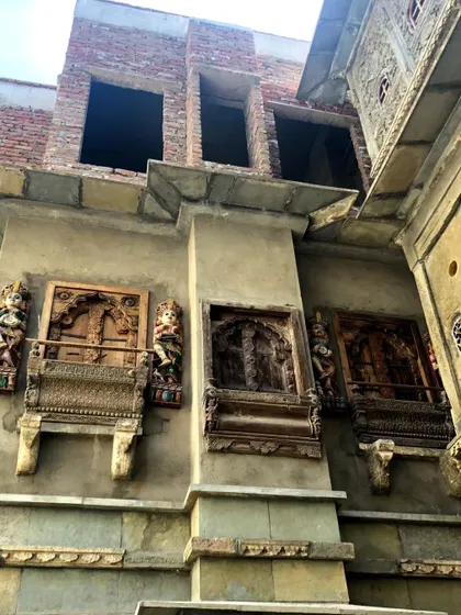 The facade of a building under restoration, showcasing a blend of new brickwork with salvaged traditional carved wooden windows. This reflects our approach to adaptive reuse and heritage conservation.