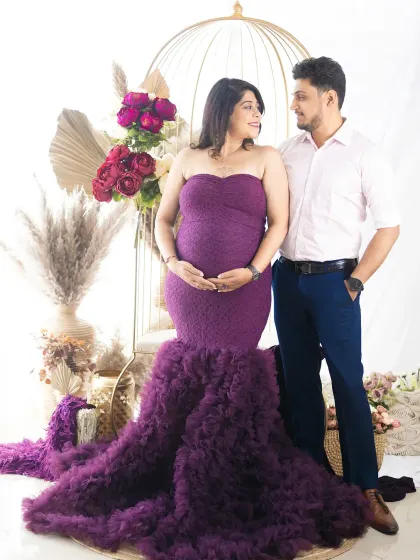 A beautiful portrait of an expecting couple. The mom-to-be is seated, wearing a stunning purple gown, creating a look of regal elegance.