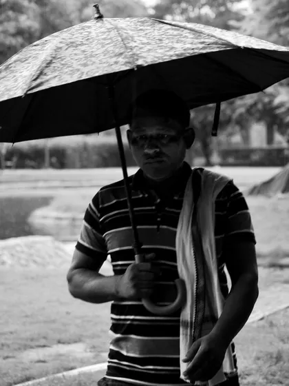 A man holds an umbrella, his face partially in shadow. This black and white street portrait has a serious, contemplative mood, telling a different kind of rainy day story.