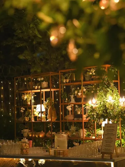 A dreamy, through-the-foliage shot of the bar and decor setup. This perspective makes the scene feel even more enchanting and secluded.