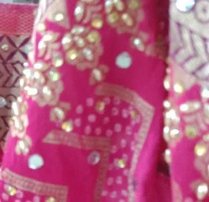 A detailed look at the mirror and thread work on a bright pink fabric. I take pride in the fine details that make each outfit unique.