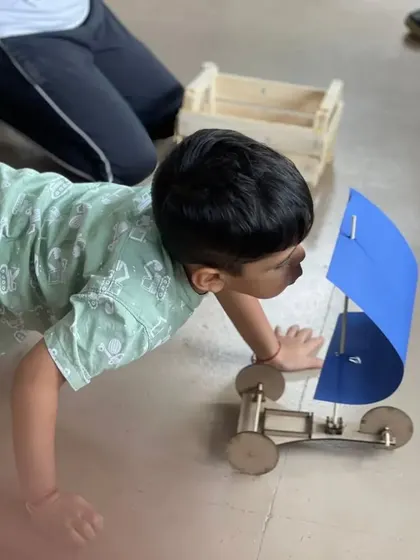 Testing the design! A young engineer gets a close look at the sail car he just built, preparing to see how well it catches the wind.