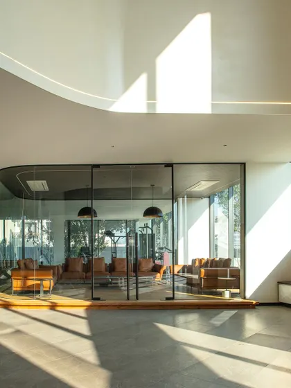This view highlights the use of curved glass walls to create a distinct yet transparent meeting or lounge area. The design allows natural light to flood the entire floor, promoting an open and collaborative office environment.