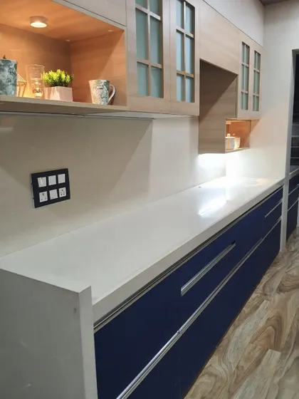A simple and elegant kitchen with royal blue lower cabinets, a white countertop, and wood-finish upper cabinets with frosted glass.