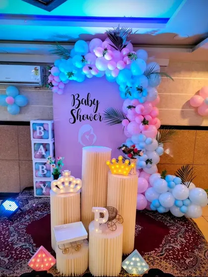 A lovely baby shower setup with a pink backdrop and a blue and pink balloon arch. The crown props and 'BABY' boxes add a touch of royalty for the mother-to-be.
