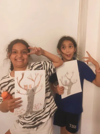 A duplicate image of students striking a pose with their finished tree artwork.