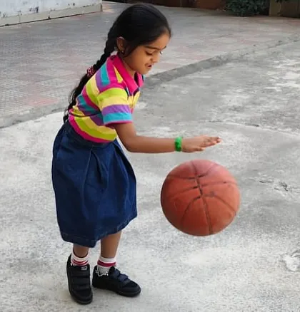 Outdoor playtime is essential for our shining stars. Here, a student practices her basketball dribbling skills, enjoying the fresh air and physical activity.