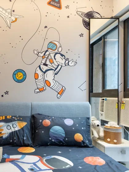 A close-up of a space-themed kids' room. The astronaut wallpaper and planet-themed bedding are easy to change as the child's interests evolve, while the furniture remains timeless.