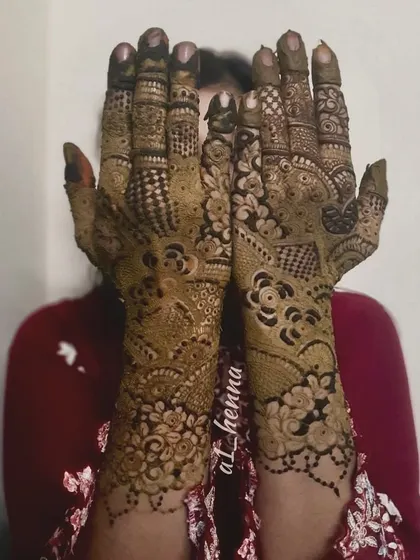 A shy pose highlighting the beautiful and dense henna work covering both hands.