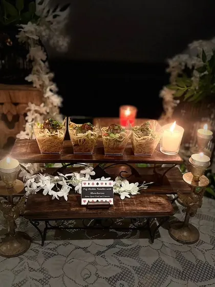 The ambient lighting from candles highlights our Veg Hakka Noodles with Manchurian, beautifully presented on a rustic wooden stand for a Diwali celebration.