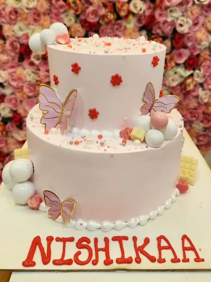 A two-tiered baby pink cake with delicate butterfly accents and sphere decorations. This Chocoholic Forest flavor cake is as delicious as it is beautiful.