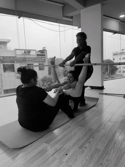 A fun, black and white shot of a partner stick yoga pose. The smiles show that practice can be both challenging and playful.