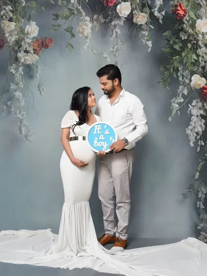 A fun gender reveal shot for a baby boy. The couple looks at each other with love while holding an "It's a boy" sign in our classic floral arch setup.