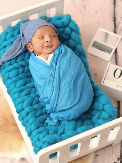 A sweet smile in his sleep. This cozy shot features a baby swaddled on a miniature bed, a perfect example of a classic, prop-based newborn portrait.