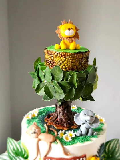A close-up of the top of the rotating jungle cake. The top tier is designed to look like a treetop, with a lion sitting proudly on it.
