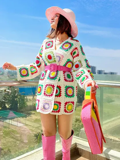 A full-length view of the crochet cardigan styled as a dress. The pink boots and belt tie the whole look together.