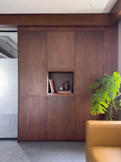 Detail of the custom, floor-to-ceiling walnut storage unit in an executive office. The seamless, handle-free design includes a central niche for display, combining practical storage with minimalist aesthetics.