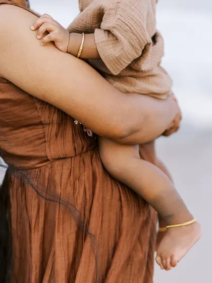 A close-up on the details of a mother holding her child on the beach. The textures and colors create a beautiful, artistic shot.