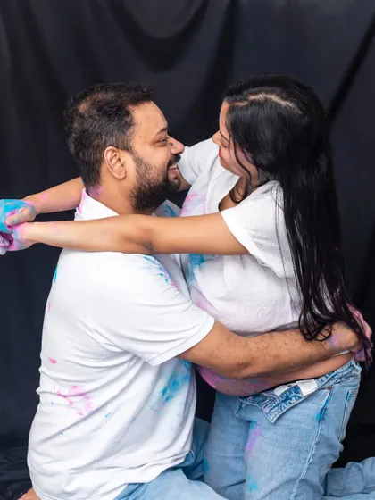 A playful and colorful studio shot. The couple's embrace, combined with the fun of the holi powder, creates a unique and joyful memory from their maternity session.