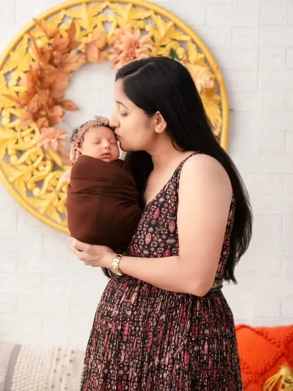 A mother gently kisses the forehead of her sleeping newborn, held lovingly in her arms. This is a portrait of pure maternal love, showcasing the soft, emotional moments we capture in our warm and comfortable studio setting.