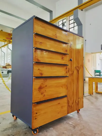 A side view of the student-made cabinet, showing the contrast between the dark grey panel body and the warm, natural grain of the finished pine wood.