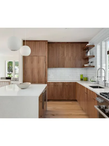 A modern kitchen featuring a white island countertop and warm wood cabinets. The open-shelf design and white subway tile backsplash add a touch of contemporary farmhouse style.