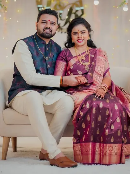 A formal portrait of the engaged couple seated together against a beautifully decorated floral backdrop. They hold hands, smiling for the camera, marking their special day.