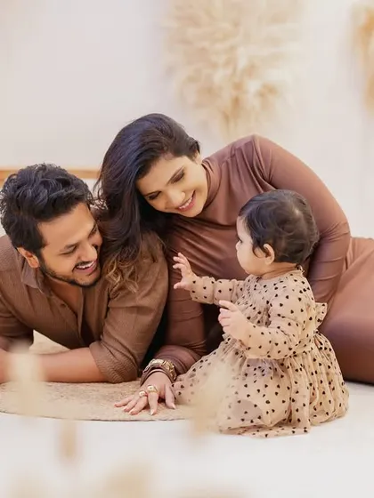 A playful, interactive moment on the floor. The parents lie down and engage with their daughter, who is pointing and exploring, showcasing the fun and candid style of my family photoshoots.