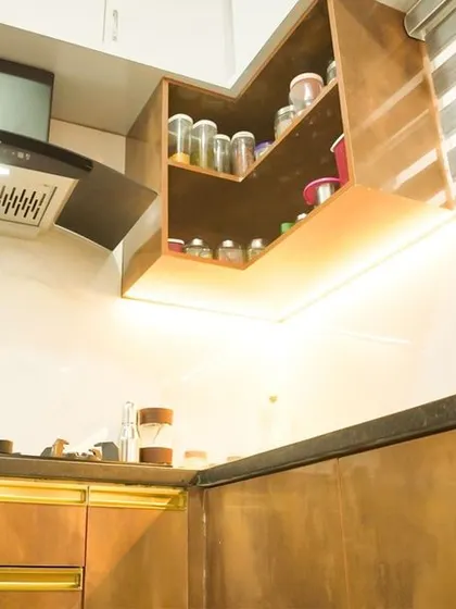 This L-shaped kitchen features a luxurious feel with its metallic bronze-finish cabinets and gold-tone profile handles. The design is complemented by a white marble-effect backsplash and warm under-cabinet lighting.