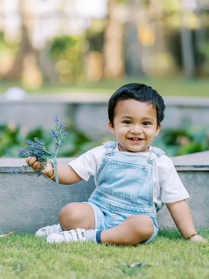 A happy baby boy in denim overalls, holding a sprig of lavender. Even the simplest props can bring out a child's curiosity and smiles.