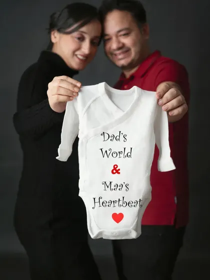 A creative and heartfelt announcement. This couple holds up a onesie that reads "Dad's World & Maa's Heartbeat," a beautiful expression of their love.