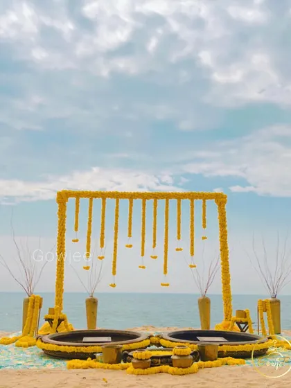 A stunning beachside Haldi setup featuring a frame with hanging marigolds against the backdrop of the sea and sky.