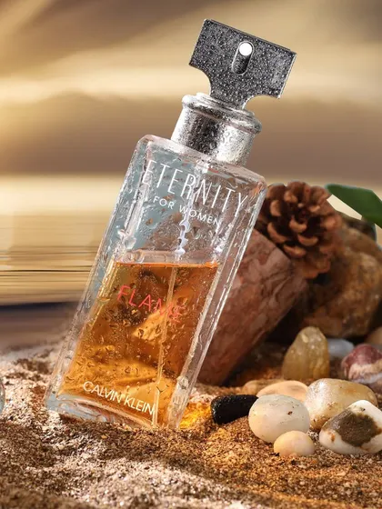A creative product shot of a Calvin Klein perfume bottle on a sandy beach at sunset, telling a story of summer and escape.