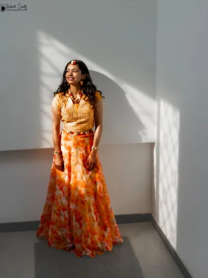 A bride in her orange and yellow Haldi lehenga, bathed in sunlight. The natural light creates beautiful shadows, adding depth and an artistic touch to this happy portrait.