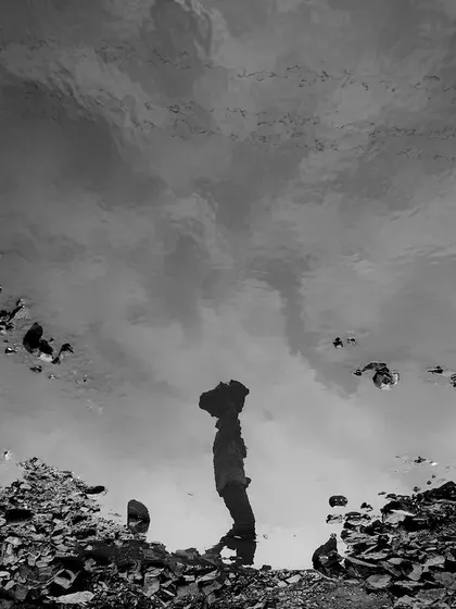 A worker's reflection is captured in a puddle at the brick kiln. This creative, black and white shot offers a different perspective on labor and identity.
