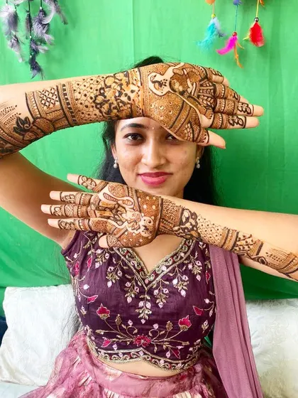 A beautiful bride framing her face with her hands, showing off a detailed design that includes elephants and other traditional patterns.
