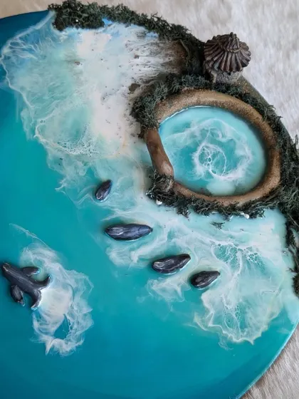 A close-up of a finished resin ocean piece, showcasing the tiny details like the hut, mossy rocks, and a dolphin swimming in the turquoise water.